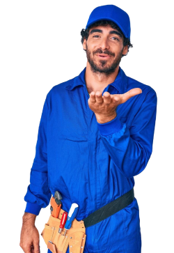 A maintenance worker in blue coveralls and cap, wearing a tool belt, making a welcoming hand gesture.